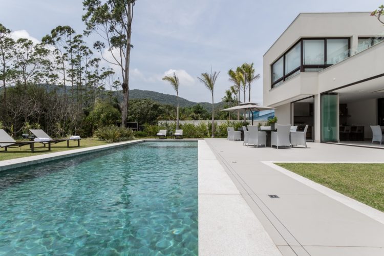 Casa com uma aréa externa bem grande e na fente uma piscina em formato retangular grande.