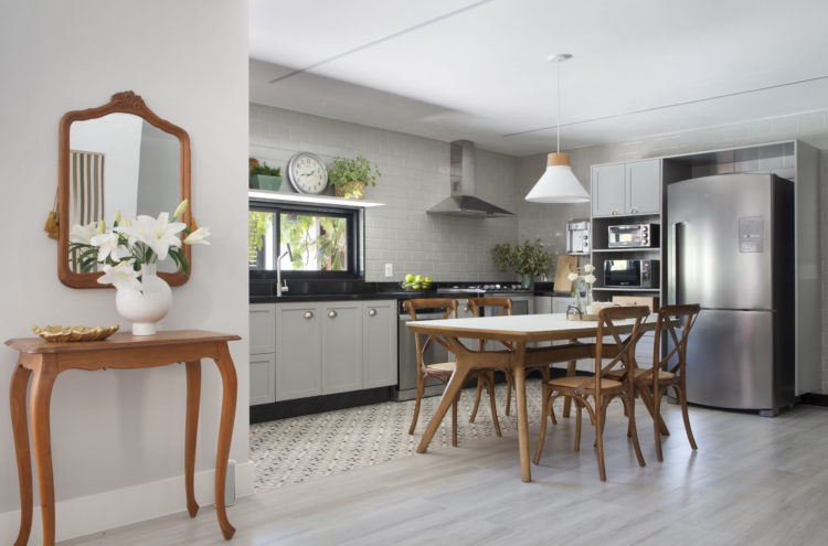 Cozinha integrada a sala de estar, divisão no piso que tem de um lado réguas de madeira clara e no pedaço molhado, azulejo hidráulico bege