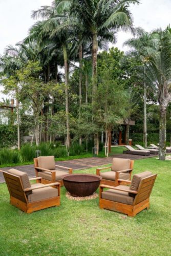 jardim com palmeiras, e no meio do gramado quatro cadeiras com uma lareira no centro