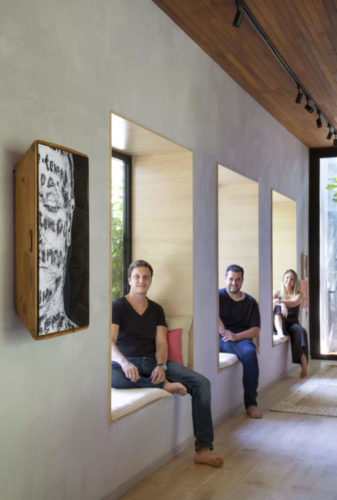 Foto do trio de arquitetos do escritório UP3 Arquitetura, cada um sentado e uma janela com banco 