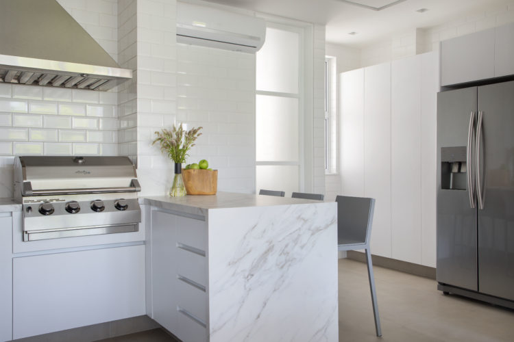 Cozinha revestida com azulejo retangular branco chamado metro , e armários e bancada branca. Uma churrasqueira instalada na bancada