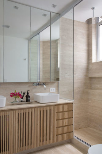 Banheiro revestido em porcelanato imitando mármore, armário embaixo da bancada em madeira ripada.