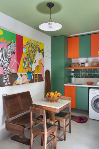 Cozinha com armários na cor laranja e verde, teto pintado de verde e moveis antigos em madeira na copa