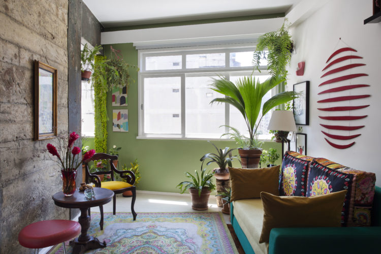 Loft com um parede descascada, parede das janelas na cor verde e o piso em porcelanato.