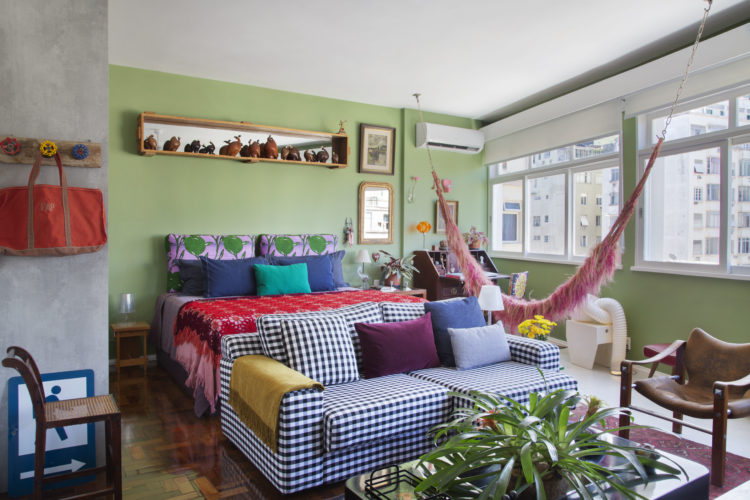 O estilo "de tudo um pouco" no novo apartamento do arquiteto Francisco Palmeiro. Espaços integrados, em frete a cama um sofá com tecido xadrez, uma rede rosa e a parede de fundo verde