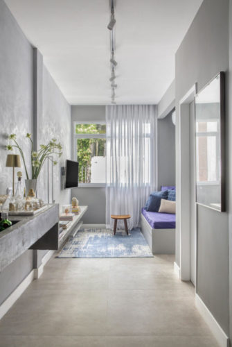 Apartamento compacto - 36m2 muito charmoso. Paredes na cor cinza imitando cimento, ao fundo na lateral espaço para um sofá que funciona como cama de hóspedes. 