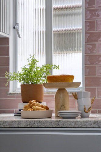 Vaso de barro com planta, um bolo em uma parto de bolo em madeira e xicaras brancas com assas douradas