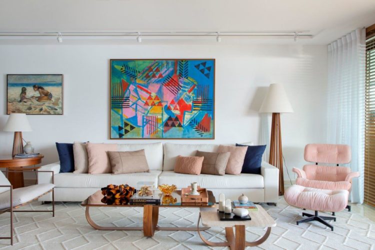 Sala clara, paredes brancas, sofá e tapete bege, poltrona charles eames na cor rosa. e em cima do sofá quadro colorido de Burle Marx