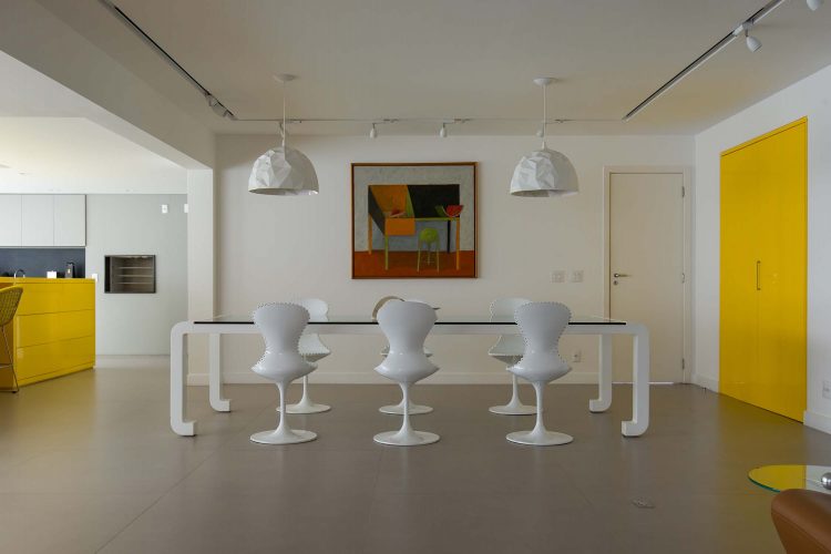 Sala bem ampla, com mesa de jantar em tampo de vidro e pés brancos, cadeiras brancas, porta de entrada dupla pintada de amarelo