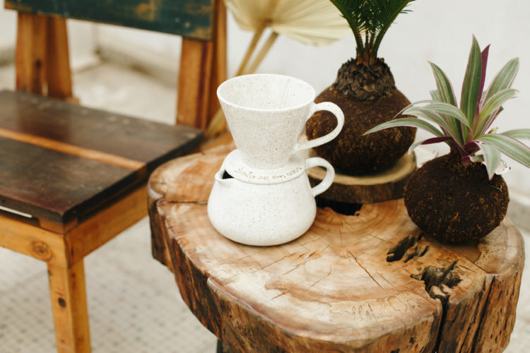Mesinha em tronco de madeira, e em cima, duas Kokedamos, arranjos florais e um bule de café me cerâmica