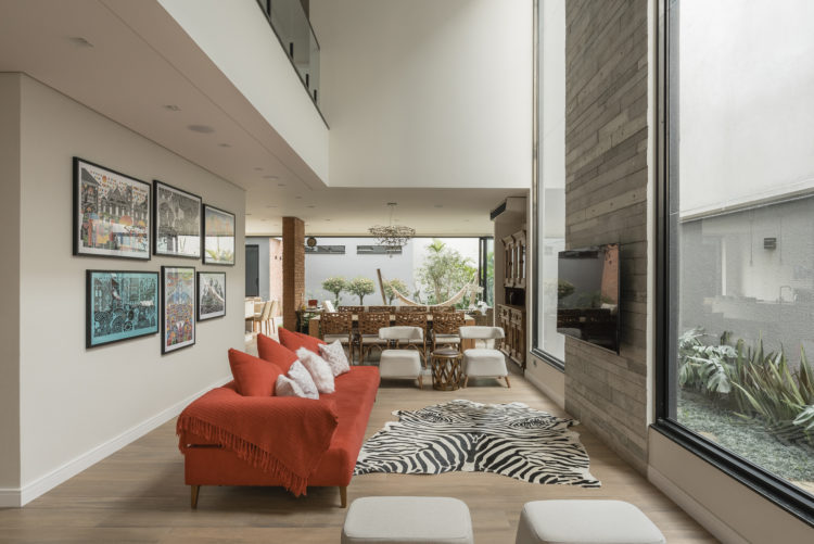 Decoração em diversos estilos nessa living com sofá vermelho, tapete de zebra e painel de porcelanato imitando madeira.