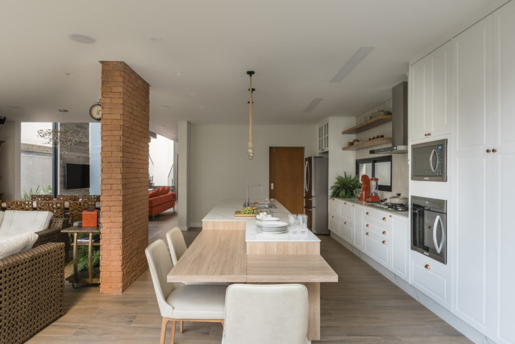 Cozinha totalmente integrada com a sala, armários brancos em estilo provençal, banca em ilha com cuba e mesa acoplada. 