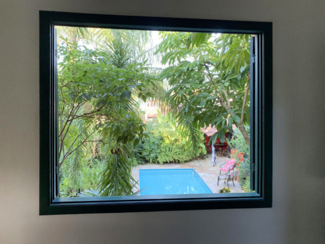 Foto de uma janela com vista exterior, para a piscina e o jardim , parecendo um quadro