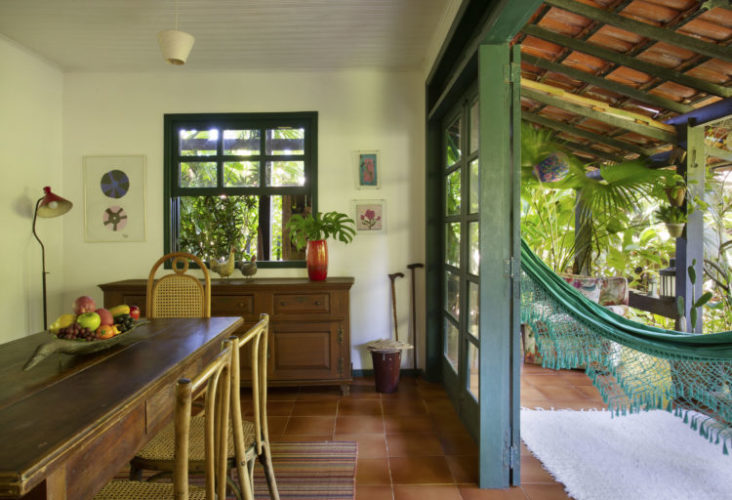 Sala de jantar em uma casa na região dos lagos, esquadrias verdes abertas para a varanda, teto de telhas e rede verde pendurada