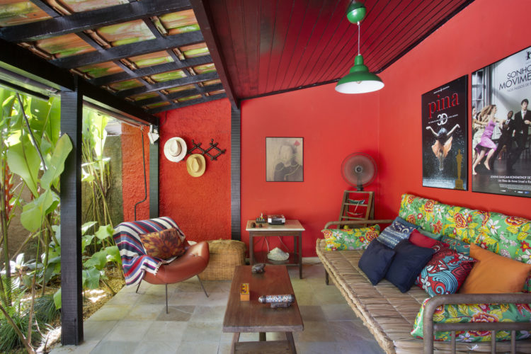Varanda aberta , com as paredes pintadas na cor laranja, sofá com almofadas na estampa de chita, floral e colorida