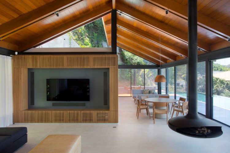 Casa na serra com projeto minimalista. Piso em concreto, uma lareira preta suspensa, teto em madeira.