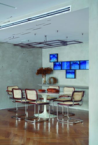 Sala de jantar com paredes na cor cinza, composição de quadros azuis em cima do aparador cinza, mesa oval Saarinen com tampo em mármore, cadeiras em palhinha.