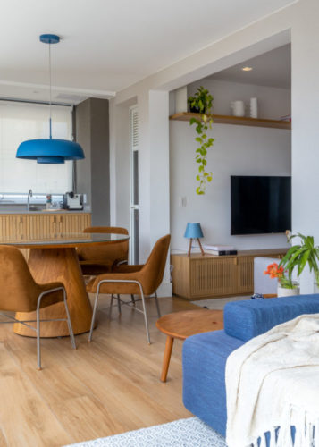 Varanda integrada no apartamento de 90m² na Zona Sul carioca. Sofá azul, mesa redonda com cadeiras em couro