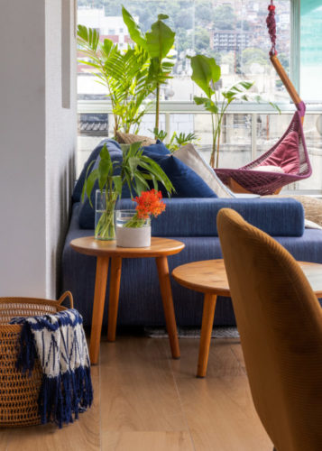 Na varanda, sofá azul, ao fundo cadeira de balanço pendente