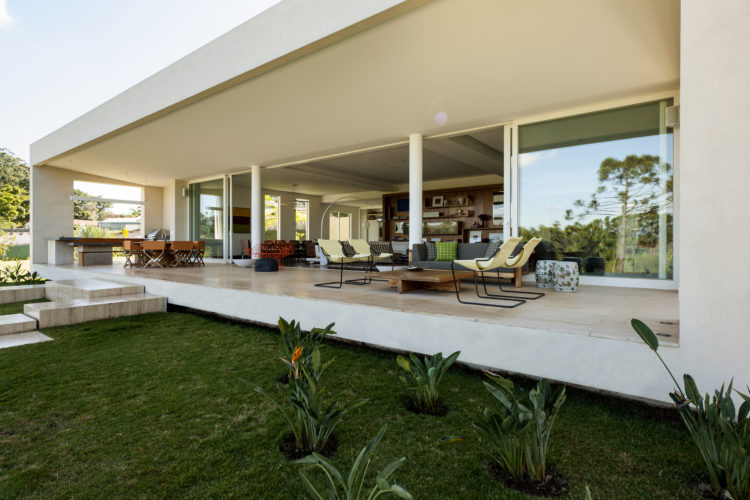 Varanda da casa em formato de um bloco retangular, com grandes painéis de vidros e portas de correr.