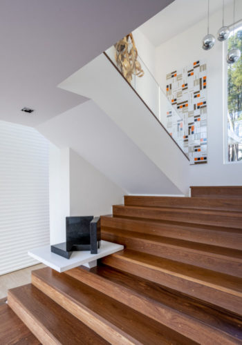 Escada em madeira com uma prateleira branca no meio que abriga uma obra de arte de Amilcar de Castro, no patamar, um painel de azulejos de Noel Marinho. 