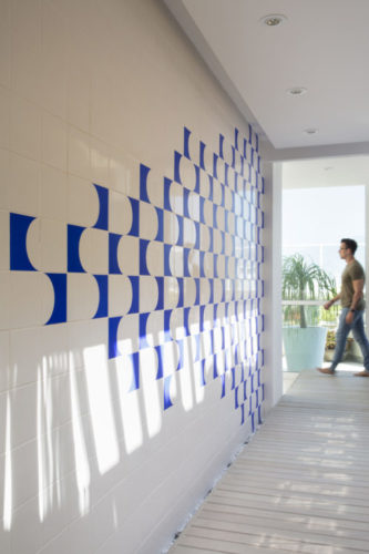 área de circulação de um segundo andar da cobertura, corredor com uma parede lateral revestida com um painel de azulejos na cor azul e branca. 