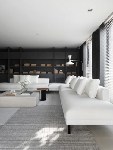 Ambiente decorado, sofá branco e grande em L , ao fundo, estante preta.