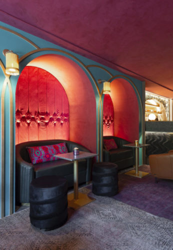 Ambiente com nichos em arco, parede vermelha de fundo, mini sofá e mesinha na frente, clima de bar