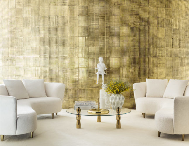 Ambiente de Brunete Fraccaroli na CASACOR SP 21, uma parede curva dourada feito em latão divide os ambientes. Na frete, dois sofás bancos e curvos sob o tapete também branco.