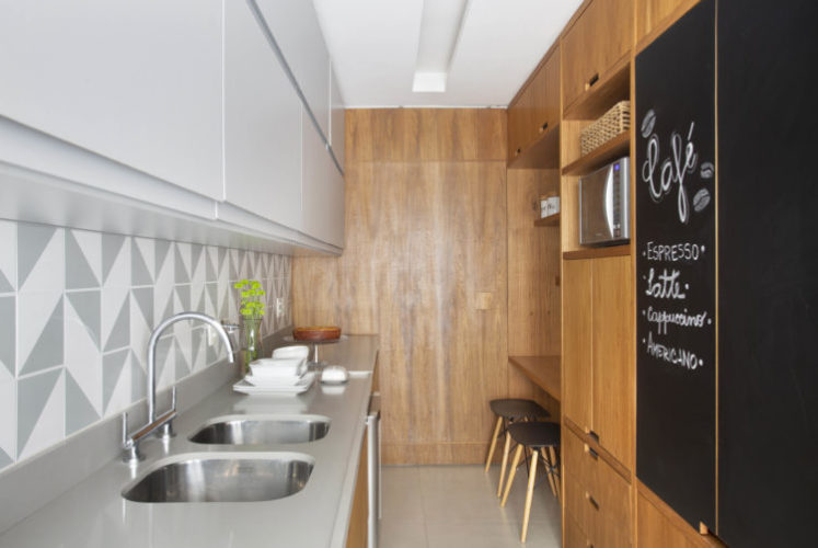 Cozinha com planta em corredor, ao fundo, porta de correr em madeiro freijó para integrar ambientes. Armários da cozinha na mesma madeira.