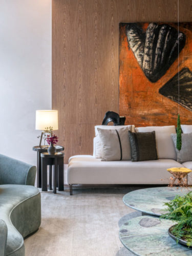 Parede forrada em madeira, em frente um sofá na cor cinza e uma tela abstrata