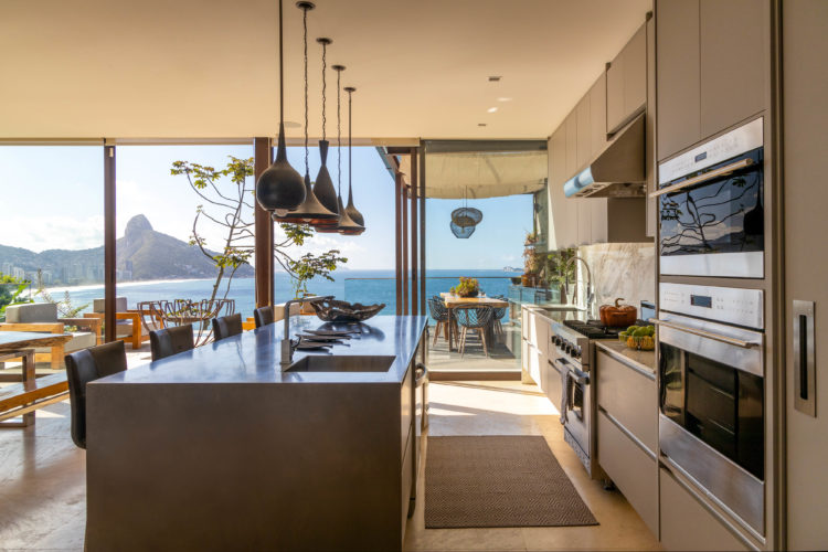 Cozinha integrada a sala, ampla e clara com panos de vidro com vista para o mar