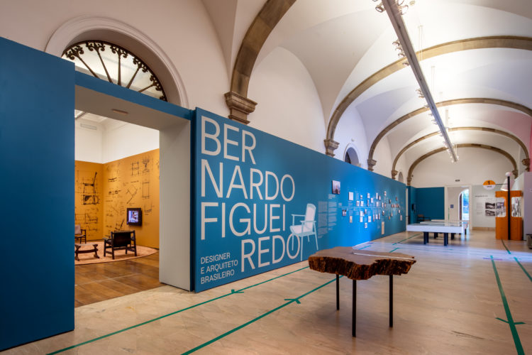 Corredor com um grande painel azul na abertura da exposição sobre Bernardo Figueiredo, designer e arquiteto brasileiro 