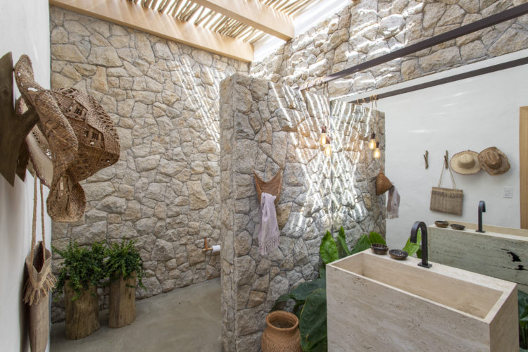 Banheiro todo revestido em pedra, cuba de mármore e iluminação natural 