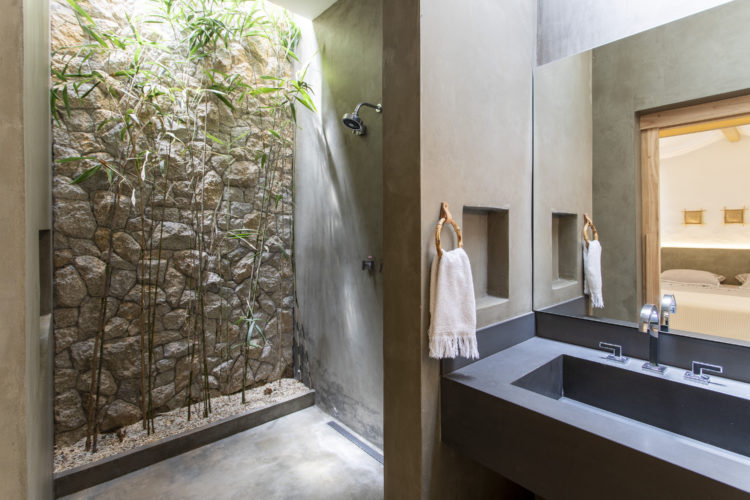Banheiro com cuba e bancada em cimento, no box. parede de pedra com bambu
