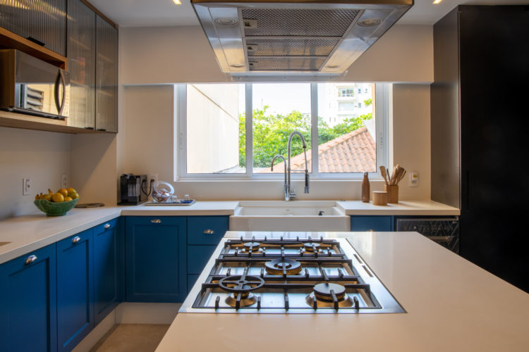 Cozinha com armários na cor azul, ilha central com fogão em cima da bancada branca.