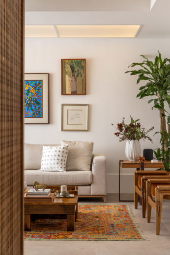 Entrada do apartamento com um painel na lateral em madeira ripada, paredes com quadro e sofá claro