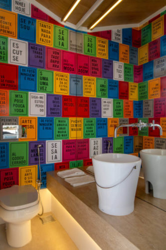 lavabo com as paredes revestidas com placas coloridas, bancada em madeira e uma balde branco em porcelana no lugar da cuba