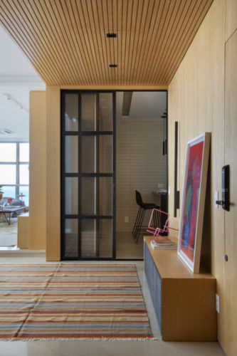 Hall de entrada com as paredes e teto forrado com madeira padrão carvalho americano, criando um efeito de caixa.