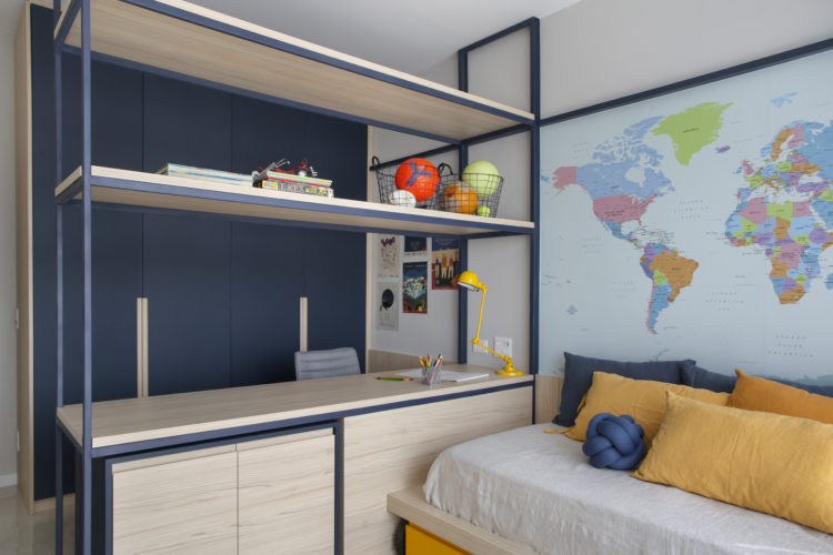 Quarto de menino, com o mapa mundi atrás da cama e uma bancada do meio do quarto, com uma estrutura de ferro e madeira em cima
