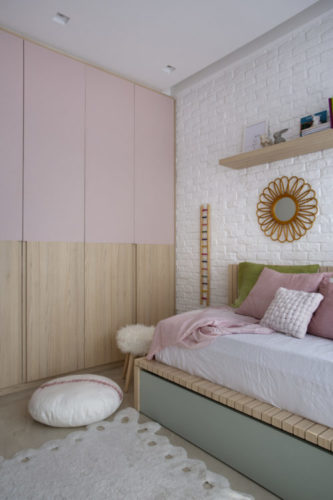 Quarto de menina decorado. Portas de armário metade em madeira e a outra metade em pintura laca rosa, parede atrás da cama om tijolinhos brancos. 