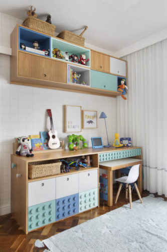 Quarto de menino decorado. Em frente a cama, nichos em madeira, bancada em madeira, embaixo , caixas organizadoras imitando lego 