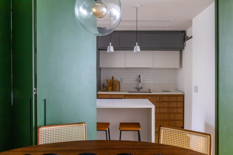 Cozinha separada da sala de jantar por porta modelo camarão pinta de verde folha, permitindo isolar ou integrar os espaços.