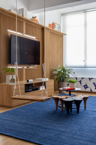 Apartamento em Ipanema com décor leve e jovem, painel ripado para a Tv , tapete azul e um balanço na sala