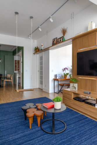Apartamento em Ipanema com décor leve e jovem, painel em madeira ripada para a tv , tapete azul e um balanço na sala