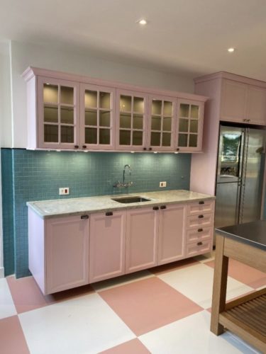 Cozinha com armários na cor rosa com fundo da parede em pastilhas verdes.