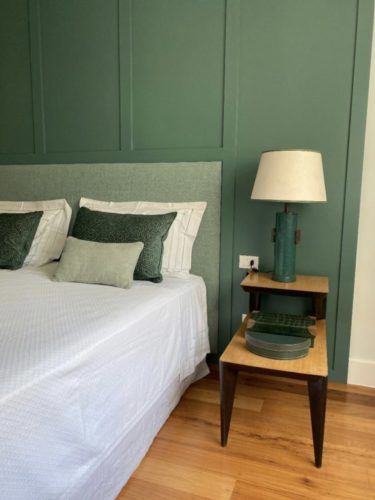 Quarto de casal com a parede atrás da cama pintada de verde , com aplicações em madeira na mesma cor.