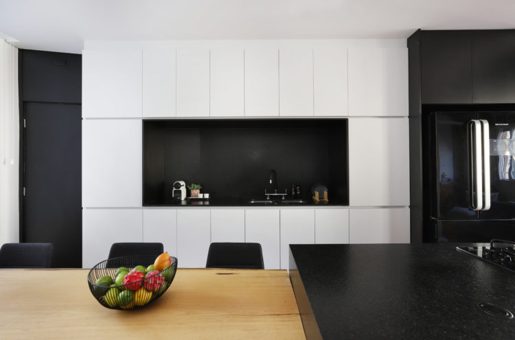 Cozinha integrada a sala, com armários brancos e um nicho preto no centro 