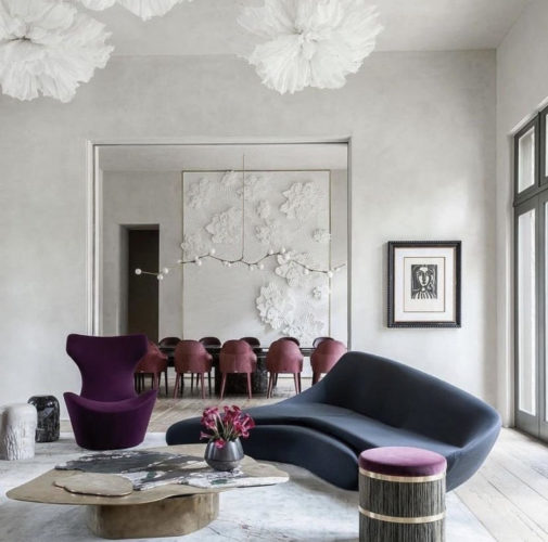A cor cinza nas paredes faz um contraste com o sofá curvo na cor azul marinho e poltrona roxa ao lado 