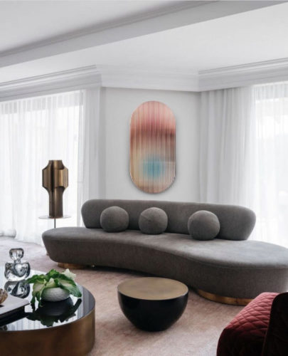 No meio da sala um sofá com forma orgânica, sem braços, apenas encosto em uma parte e com almofadas redondas 